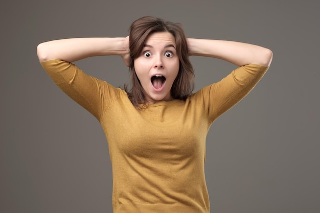 Shocked young woman with hands on head standing and shouting with surprise