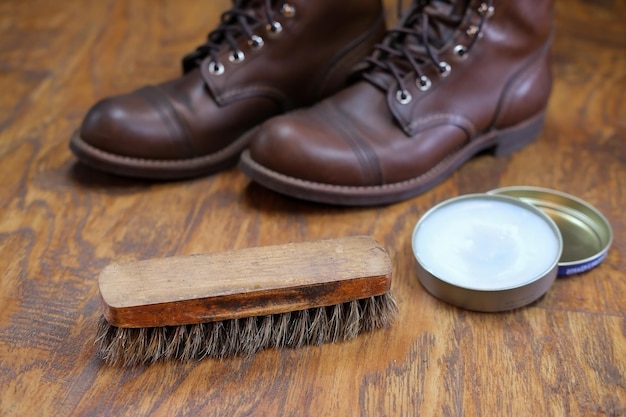 Spazzola per scarpe, olio di visone e un paio di stivali in pelle su  pavimento in legno