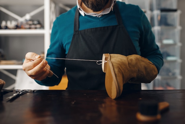 Shoemaker stitches the shoe, footwear repair service