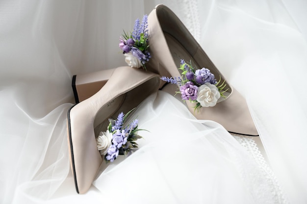 Shoes for the bride lie on a wedding dress with flowers