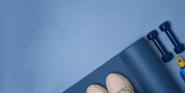 Shoes, smart phone, bottle of water, mat and dumbbells on blue background.