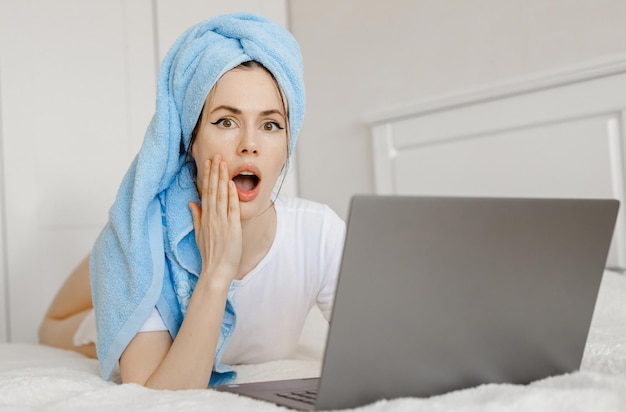 Шокированные молодые женщины с открытым ртом в очереди с ноутбуком в гостиной домаПокупки онлайн дома в банном полотенцеДомашняя работа Блокировка от коронавируса