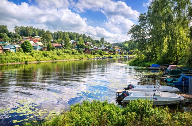 Река Шохонка в городе Плёс, деревянные старые дома с отражениями и лодки и лодки у берега в летний солнечный день