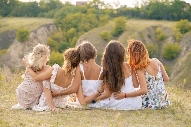 Shoot from back. The company of female friends having fun, hugs each other and enjoy hills landscape