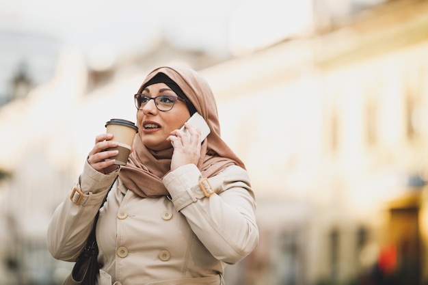 도시 환경을 걷는 동안 히잡을 쓰고 스마트폰으로 말하는 이슬람 여성의 촬영.