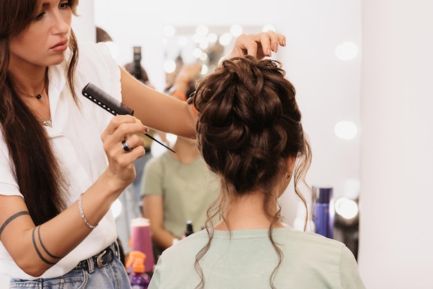 Shooting in a beauty salon A hair stylist corrects the hairstyle of a young darkhaired girl with a hair comb