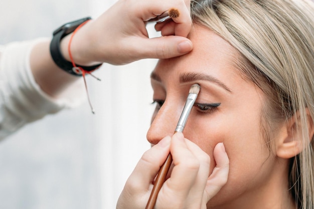 Shooting in a beauty salon a young beautiful girl model master
makeup artist applies eye shadow