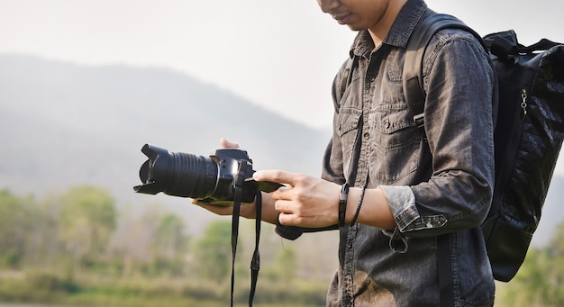 風景の景色を撮影、カメラを保持しながら若いアジアの男性写真家のクローズアップ