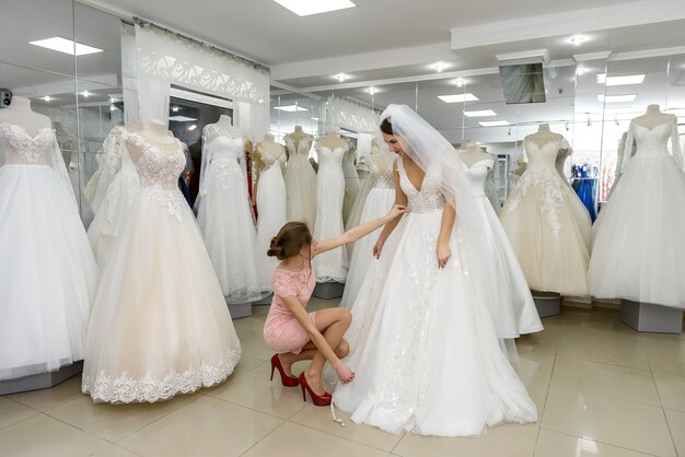 La commessa aiuta la sposa con l'abito da sposa nella boutique