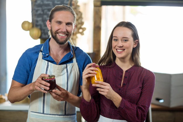 Shop assistants interacting while holding jam and pickle jar at grocery shop