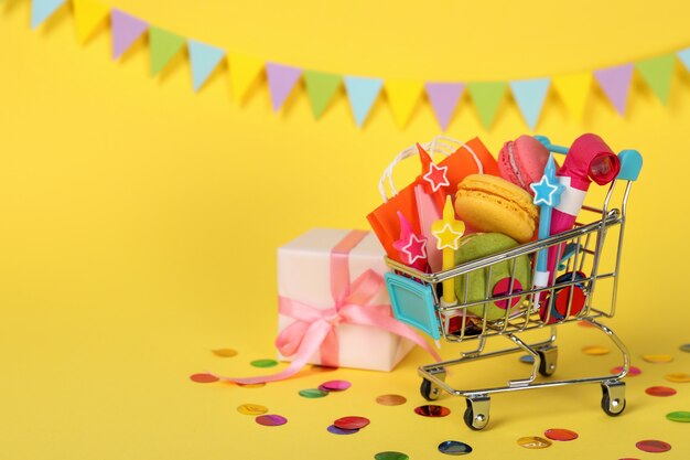 Shop cart with birthday accessories on yellow background, space for text