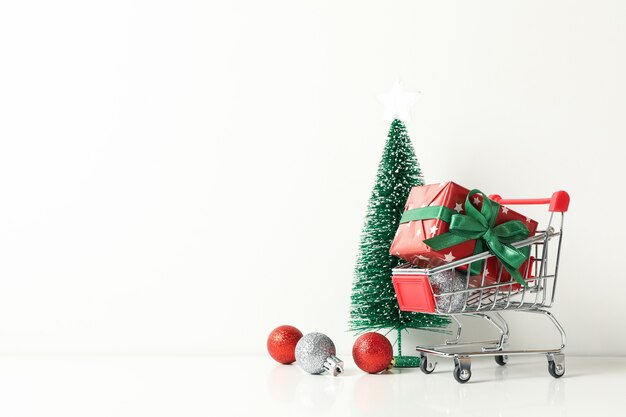 Shop cart with gift box and Christmas accessories on white table