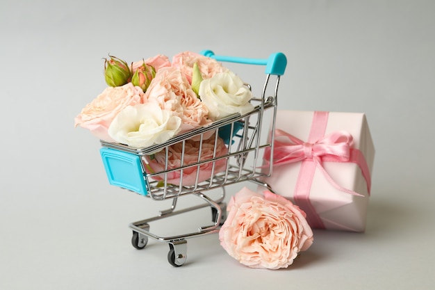 Shop trolley with roses and gift box on gray background