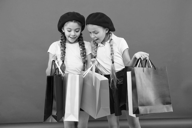 Shopaholic concept Signs you are addicted to shopping Kids cute schoolgirls hold bunch shopping bags Children pupils satisfied by shopping red background Obsessed with shopping and clothing malls