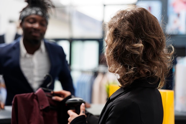 Shopaholic customer paying for fashionable clothes, making transaction on pos terminal in shopping center. Showroom manager scanning purchase using store scanner, commercial activity concept