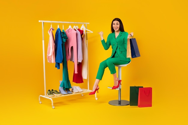 Shopaholic Excited lady pointing at colorful clothes on clothing rail shopping and choosing new outfil