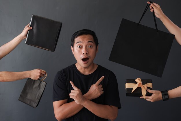 Shopaholic man surrounded by many hands holding shopping bags