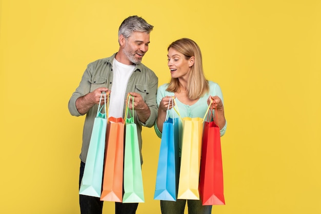 Shopaholics Overjoyed middle aged spouses holding shopping bags and looking inside excited about their new purchases