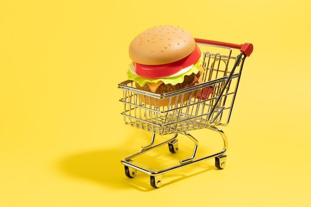 Shoping cart with a plastic burguer inside on yellow background