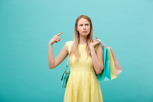 ショッピングと販売の概念：買い物袋と黄色のエレガントなドレスの美しい不幸な若い女性。