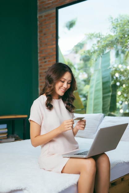 Shopper girl is buying online with a laptop and credit card sitting in nice light room