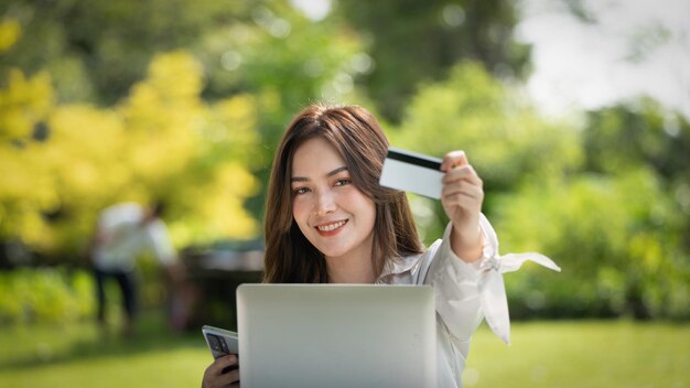 Shopper glimlach meisje online kopen of online werken met een slimme telefoon en creditcard zittend op een bankje in een stadspark in de zomer Smile meisje blij met haar kaart portret van een jonge executive
