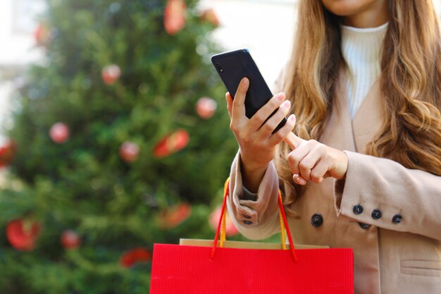 Shopper vrouw met behulp van slimme telefoon om online te winkelen en draagtassen op kersttijd.