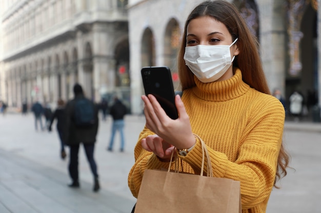 Shopper donna con mascherina chirurgica utilizzando app per smartphone in una strada cittadina