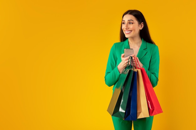 Shopping app concept happy lady holding smartphone and colorful shopper bags looking aside at free space