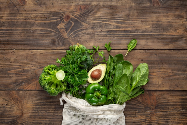 Shopping bag with green vegetables on wooden table. Purchase healthy food