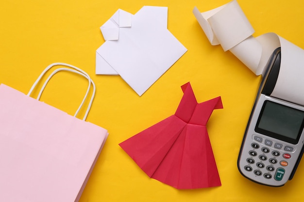 Shopping bag with origami dress and shirt payment terminal on a\
yellow background payment for purchases shopping concept