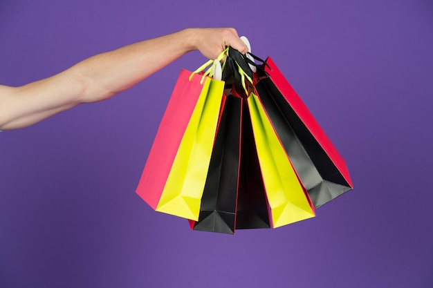 Shopping bags in hand on violet background. Paper bags of different colors. Bags or paperbags. Shopping or sale and black friday concept. Holidays preparation and celebration. Gift and present.