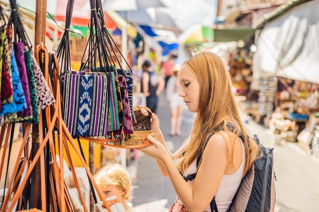 Foto shopping a bali. la giovane donna sceglie le famose borse ecologiche in rattan balinese in un mercato di souvenir locale a bali, in indonesia