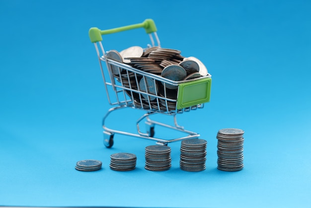 Shopping basket contains coins on blue background. Uncontrolled spending in concept stores