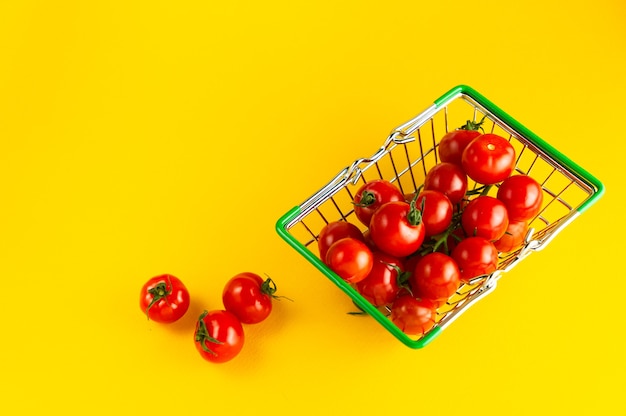 Shopping basket filled with cherry tomatoes on a bright yellow background