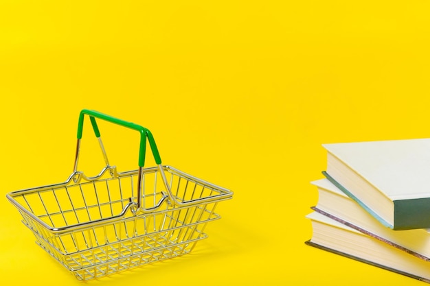 Корзина для покупок и стопка книг на желтом фоне.