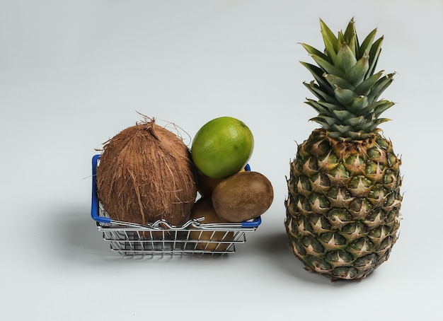 白い背景の上の買い物かごと熱帯の果物。スーパーで買い物。健康食品のコンセプト。