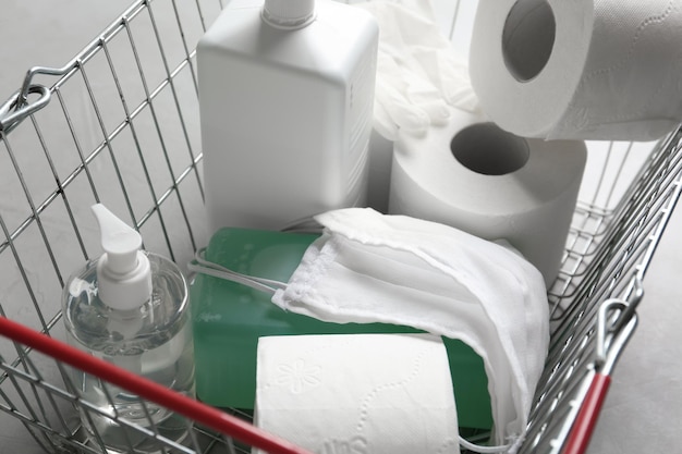 Shopping basket with antiseptics toilet paper gloves and masks on grey table closeup Panic caused by virus