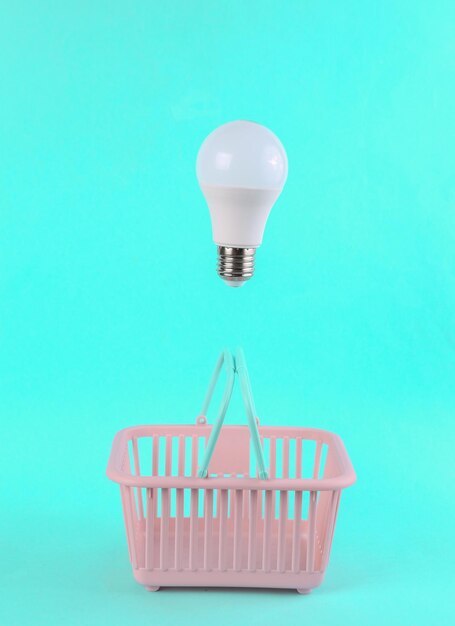 青の明るい背景に浮かぶ電球が付いた買い物かご 最小限のショッピングのコンセプト