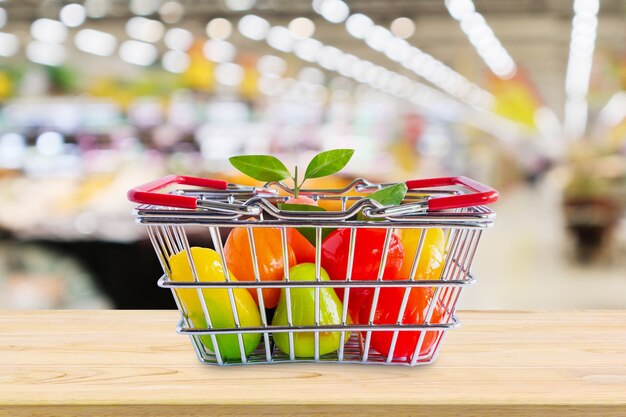 Shopping basket with fruits on wood table over grocery store supermarket