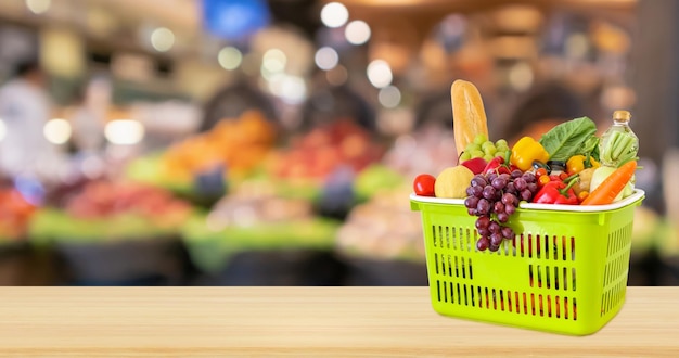 shopping basket with groceries product on wood table top with supermarket grocery store background