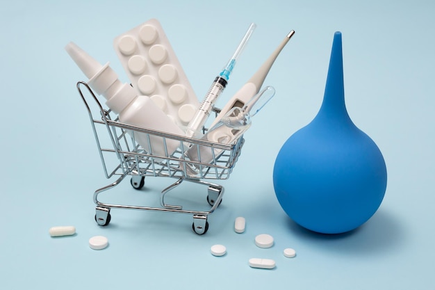 Shopping basket with medicinal pills nasal spray syringe thermometer and enema on a blue background