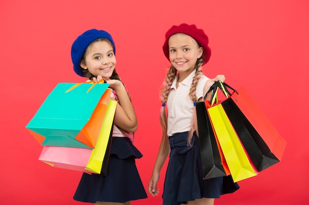 Shopping become fun with best friends. Kids cute schoolgirls hold bunch shopping bags. Children satisfied by shopping red background. Obsessed with shopping and clothing malls. Shopaholic concept.