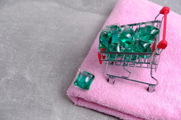 Shopping cart filled with laundry capsules stands on pink terry towel