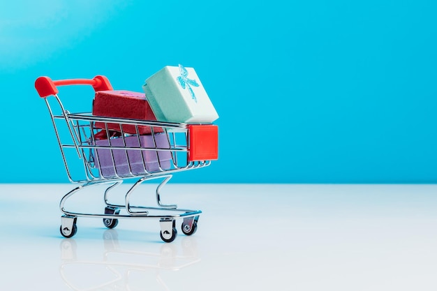 Shopping cart filled with presents isolated on blue background Christmas birthday and sale concept