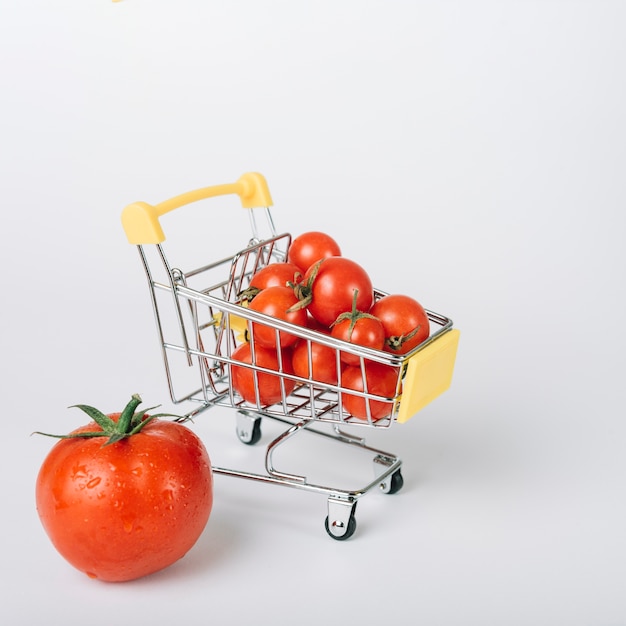 Foto carrello della spesa pieno di pomodori rossi freschi su sfondo bianco