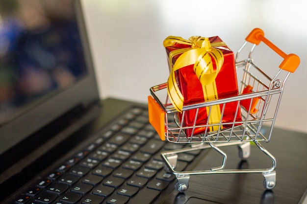 Shopping cart full of gold gift boxes and red sale sign through laptop monitor 
