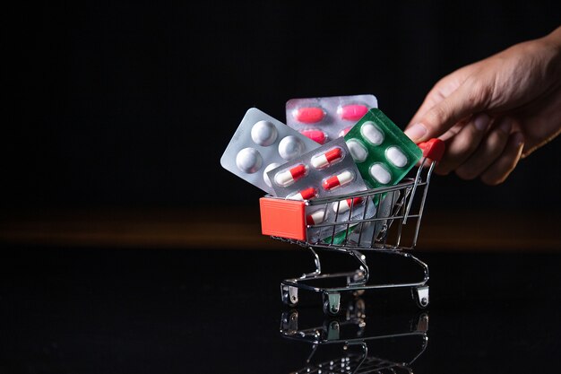 Shopping cart loaded with pills on dark background. Shopping medicine concept