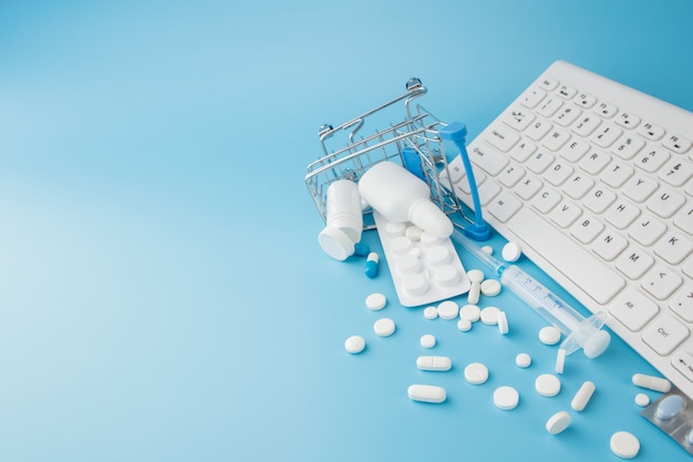 Photo shopping cart toy with medicaments and keyboard. pills, blister packs, medical bottles, thermometer, protective mask on a blue background. top view with place for your text