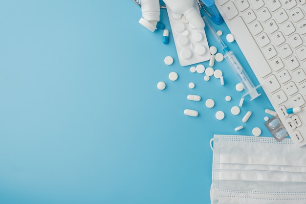 Shopping cart toy with medicaments and keyboard. pills, blister packs, medical bottles, thermometer, protective mask on a blue background. top view with place for your text